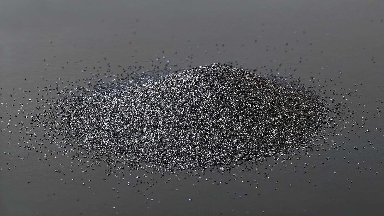 A loose pile of dark, sharply angular silicon carbide grains at 60 mesh, roughly 0.25 mm across, shown as a coarse abrasive-grade material.